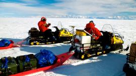 Matthew Siegfried, forefront, and seismologist Marino Protti, of the Observatorio Vulcanológico y Sismológico de Costa Rica, prepare to move equipment at Whillans Ice Plain. The Transantarctic Mountains are in the background.